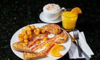A traditional bacon and eggs breakfast served with crispy breakfast potatoes, a hot cappuccino, and fresh orange juice a