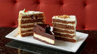 A variety of gourmet cake slices including Carrot Cake, Hummingbird Cake, and Triple Brownie Cheesecake at Symposium Caf