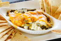 A creamy, warm spinach dip appetizer served with fresh bread, available at a great price during Happy Hour at Symposium 