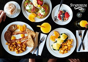 Breakfast and brunch spread with eggs Benedict, bacon and eggs, avocado toast, and fresh fruit at Symposium Cafe Restaurant in Bolton